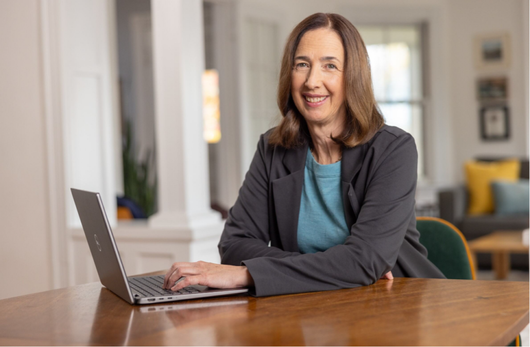 Isabelle Lousada smiling, sitting at a desk in front of a computer.